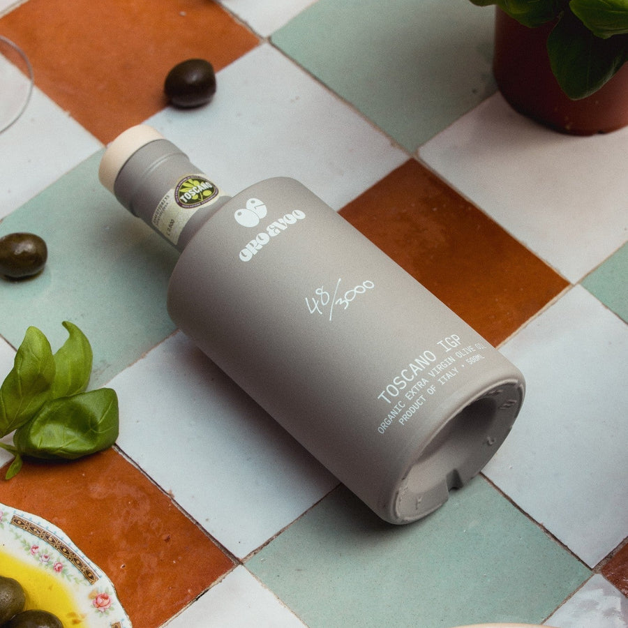 ORO bottle 48/3000 lying centred on chequered tiles with olives, basil and bread